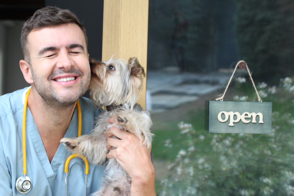 smiling veterinarian holding a dog in front of office with open sign on weekends in the background