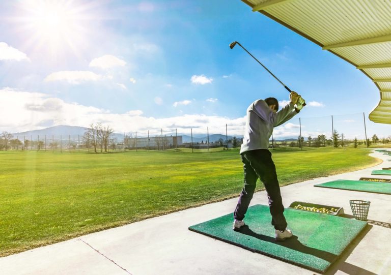 A golfer hitting a ball at a driving range with a beautiful blue sky in the background