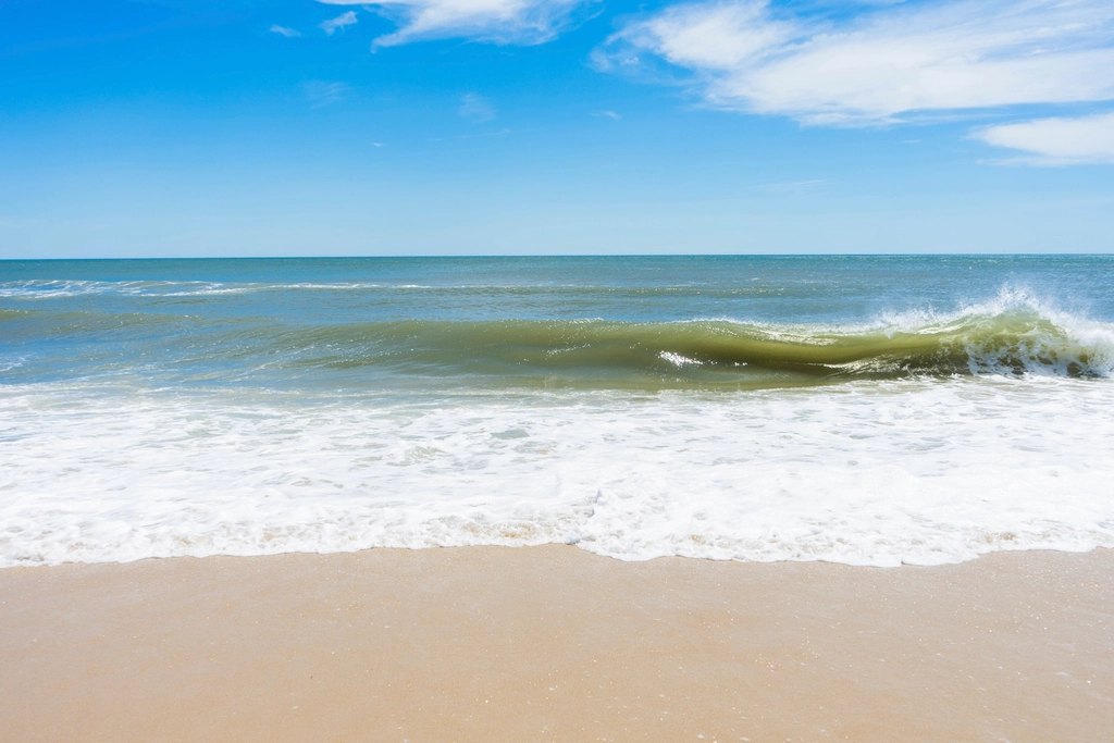 Surf breaking on a sandy beach under blue sky